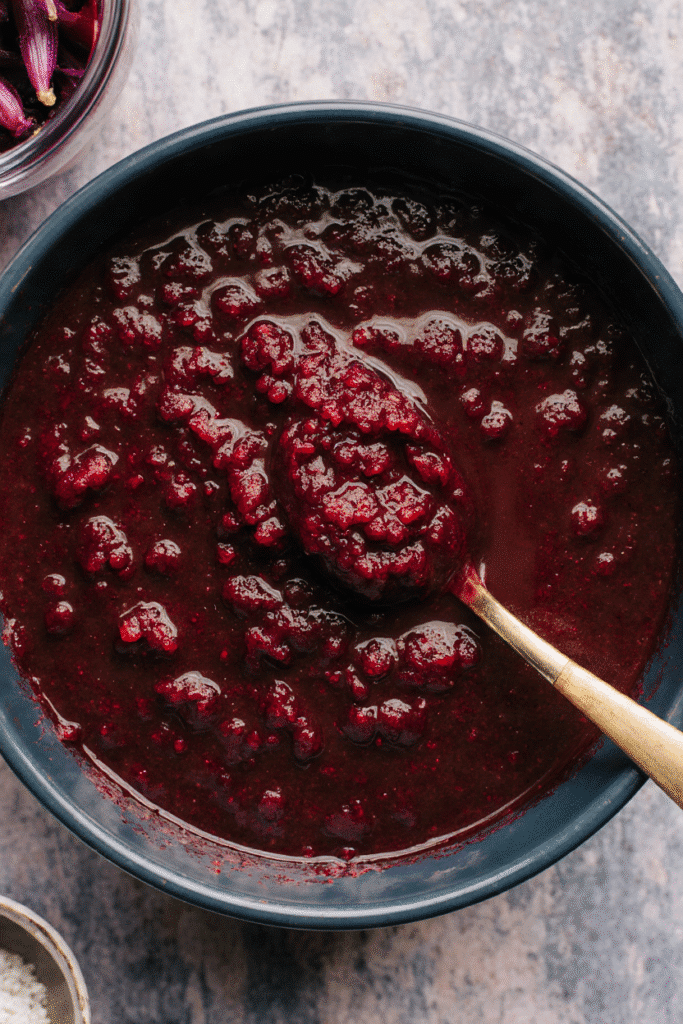 A jar of glossy, thick beetroot jam (Artisanal Preserves) next to a spoon showing its rich, deep red, jewel-like consistency.