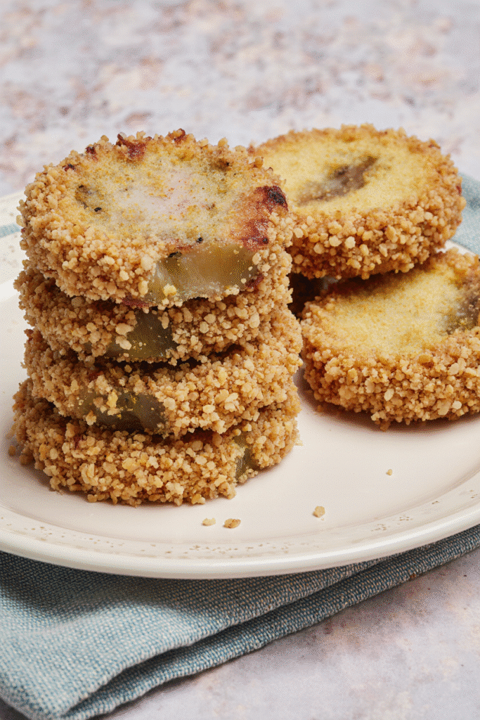 Stack of freshly fried, hot, and crispy green tomato slices sprinkled with salt.