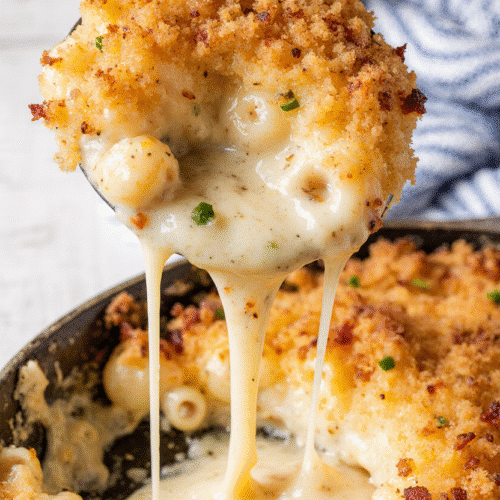 A close-up of bubbly, golden-brown smoked mac and cheese in a cast iron skillet, with a crispy breadcrumb topping