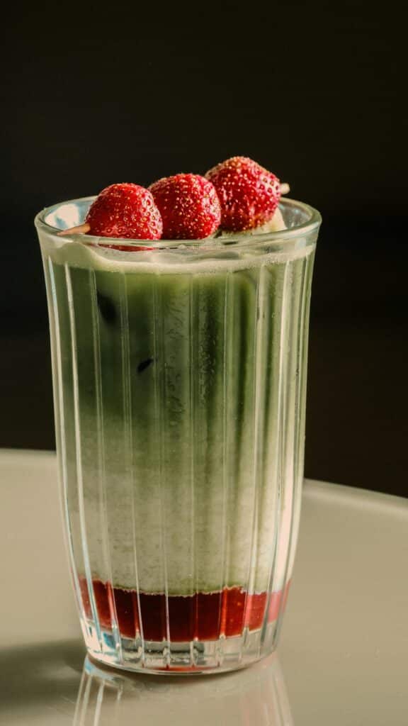 Iced matcha strawberry latte with creamy milk and strawberry puree served in a clear cup with metal straw.