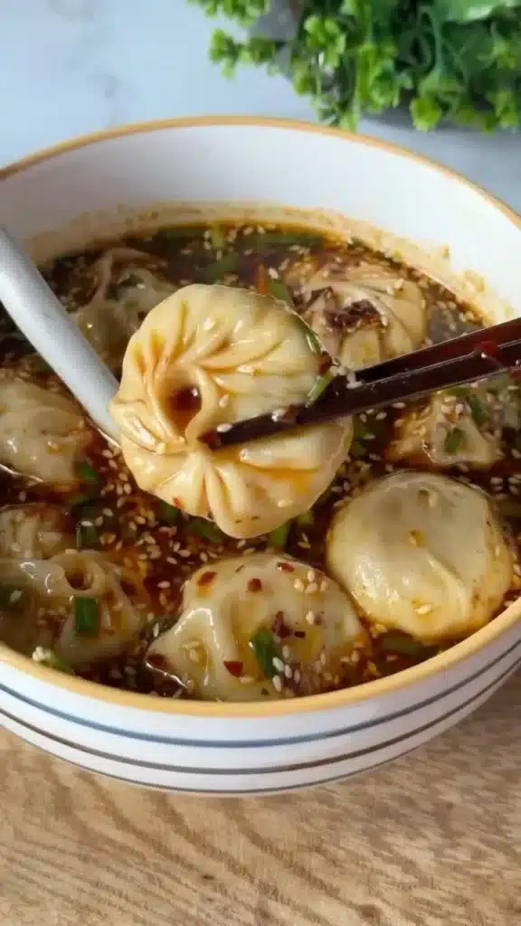 Bowl of spicy dumpling soup with fresh herbs and chili flakes