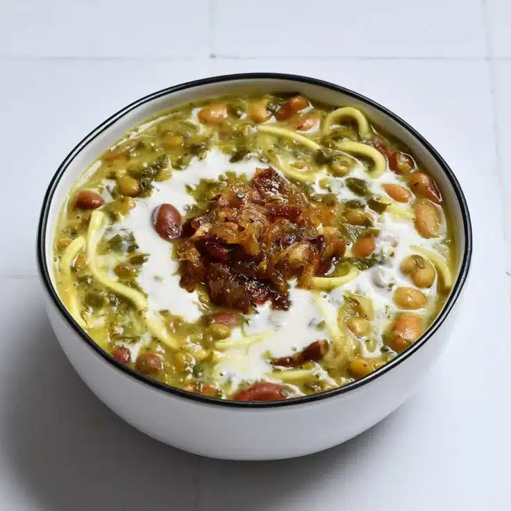 A bowl of Aash Reshteh noodle soup topped with fresh herbs and ingredients.