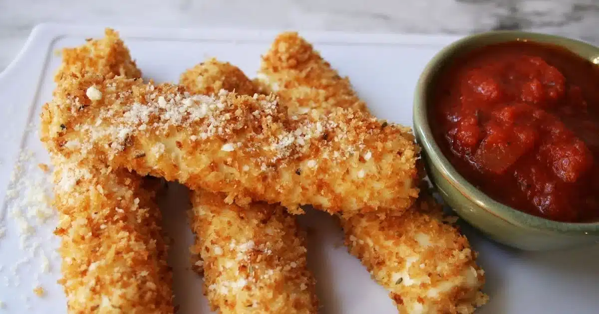 Delicious baked mozzarella sticks on a plate with marinara sauce