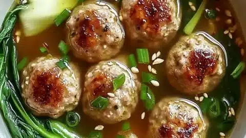 Bowl of Ginger Chicken Meatball Soup with Bok Choy and herbs for a cozy meal.
