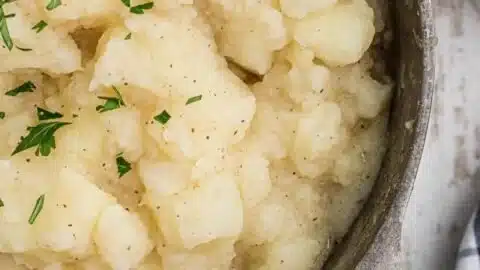 Bowl of stewed potatoes garnished with herbs, showcasing delicious comfort food.