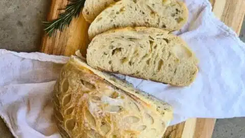 Freshly baked roasted garlic and rosemary sourdough bread loaf displayed on a wooden table.